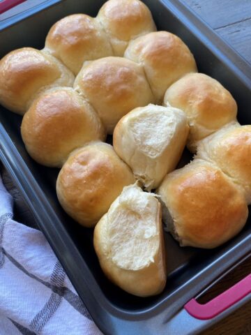 Baked Homemade Dinner Rolls in a pan with a dishtowel beside the pan.