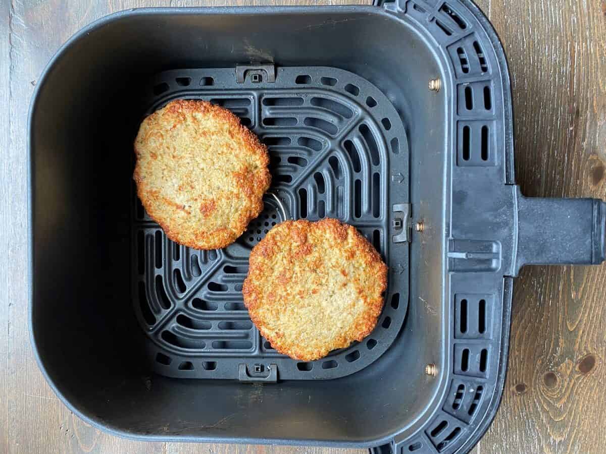 Two cooked chicken burgers in an air fryer basket.