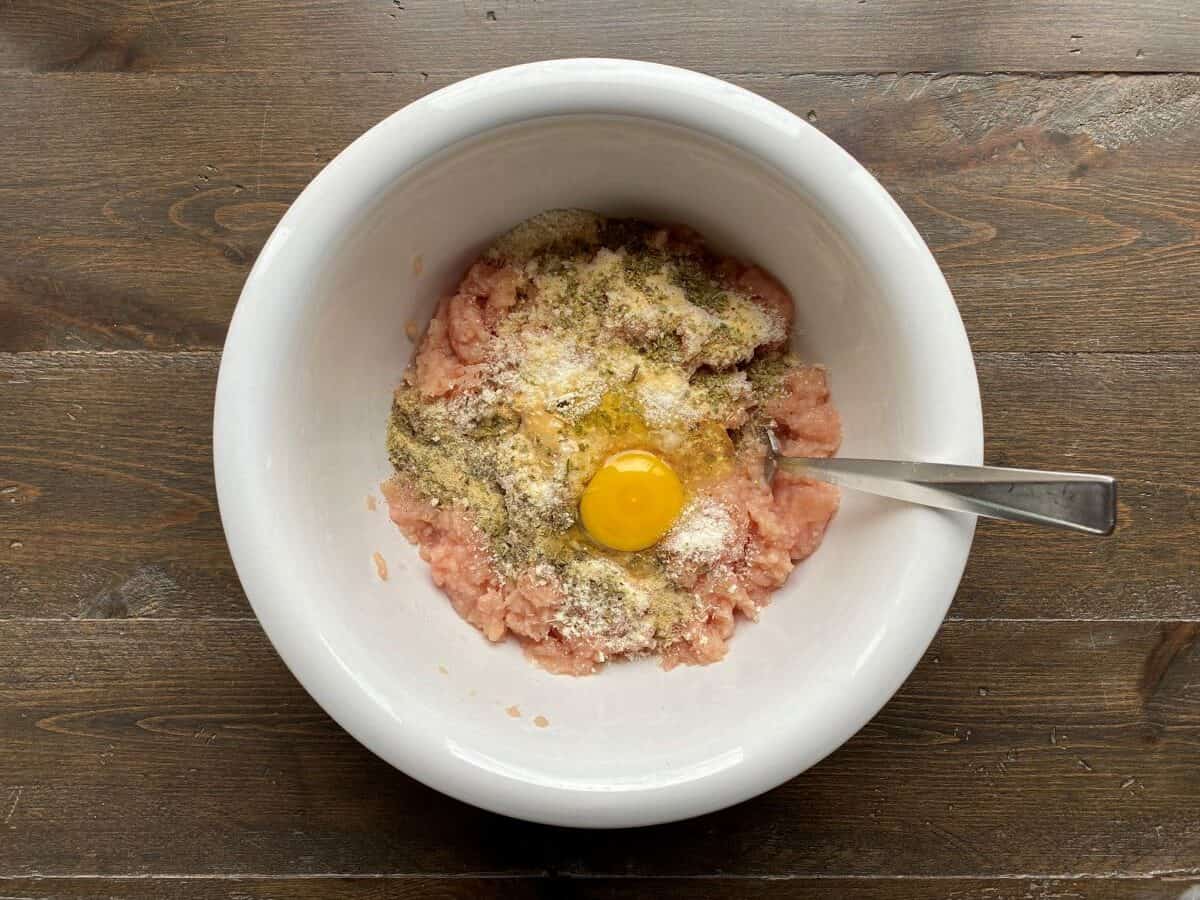 Ground chicken, parmesan cheese, egg and spices are in a large bowl.