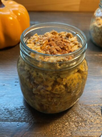 A glass jar of overnight oats in the foreground and another jar of oats and a pumpkin in the background.