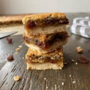 A stack of butter tart squares in the foreground and uncut butter tart squares in the background.