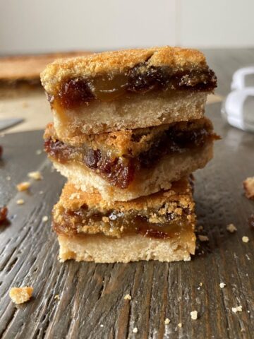 A stack of butter tart squares in the foreground and uncut butter tart squares in the background.