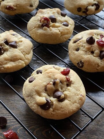 Dark chocolate cranberry cookies on a black wire rack on top of a brown wooden surface.