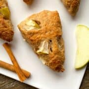 Apple scones with cinnamon sticks and an apple slice on a white cutting board.