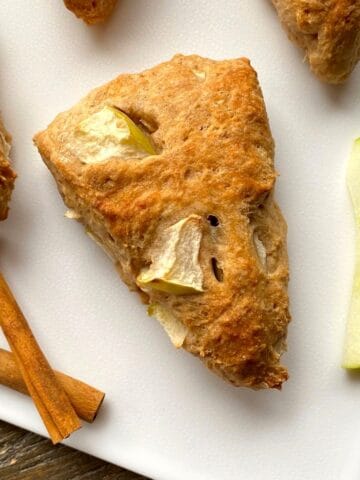 Apple scones with cinnamon sticks and an apple slice on a white cutting board.